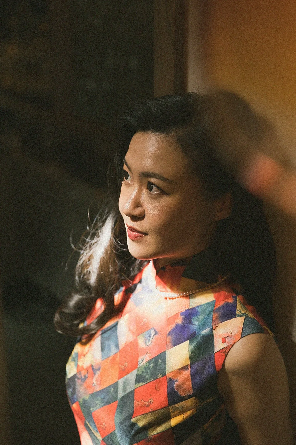 A woman with dark hair wearing a colorful, patterned sleeveless dress.