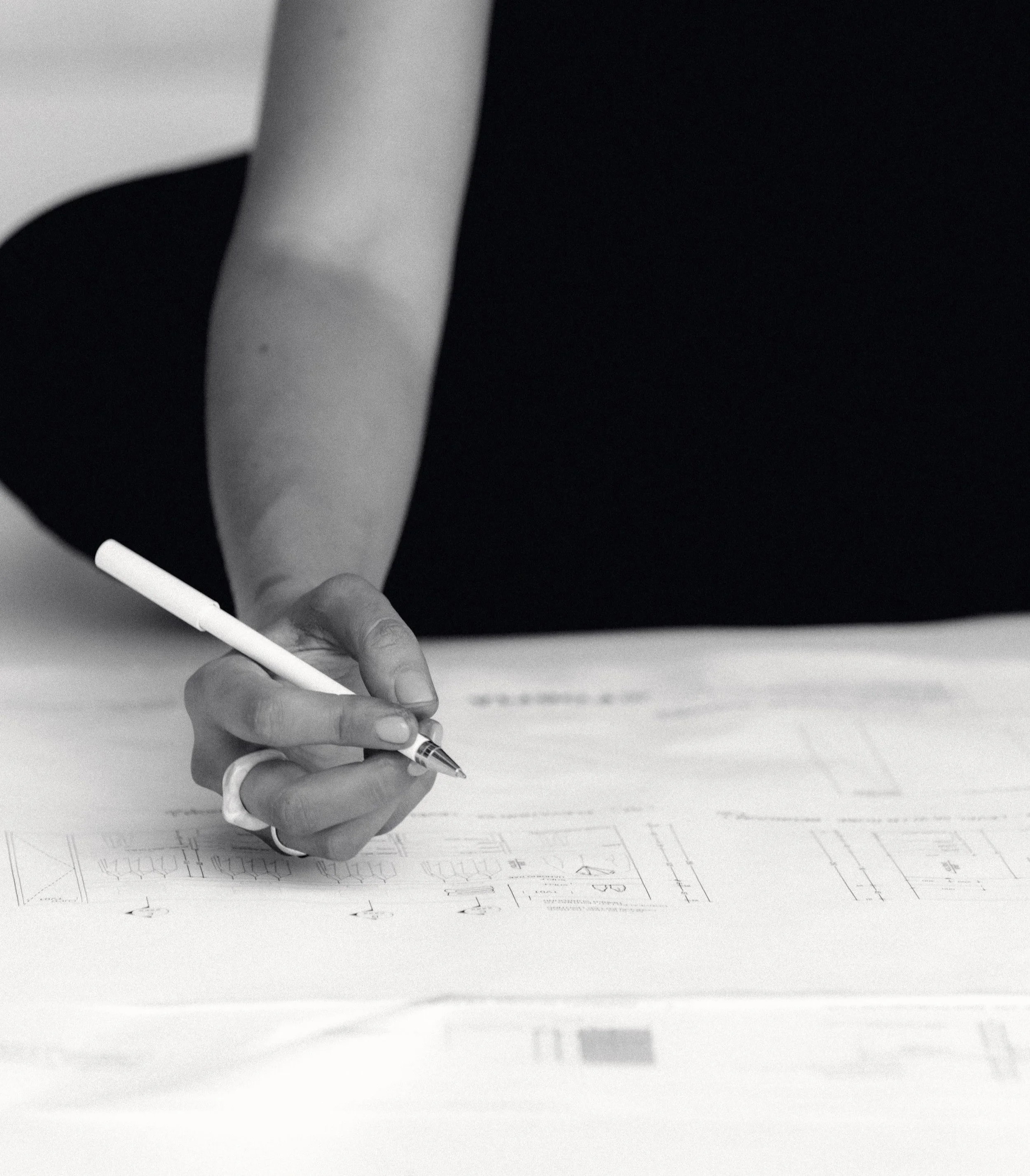A person drawing on architectural blueprints with a pen.