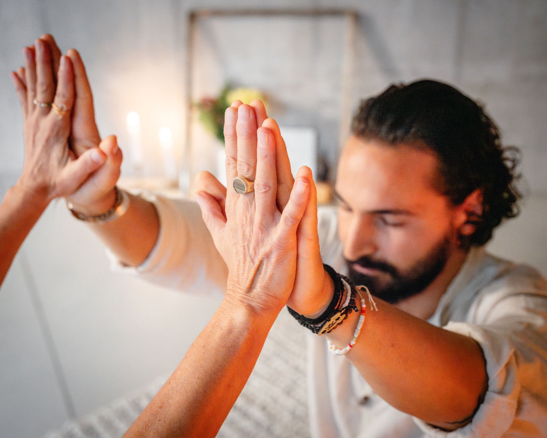 Two people practicing yoga, performing a high-five with their hands joined together, in a cozy, well-lit indoor setting.