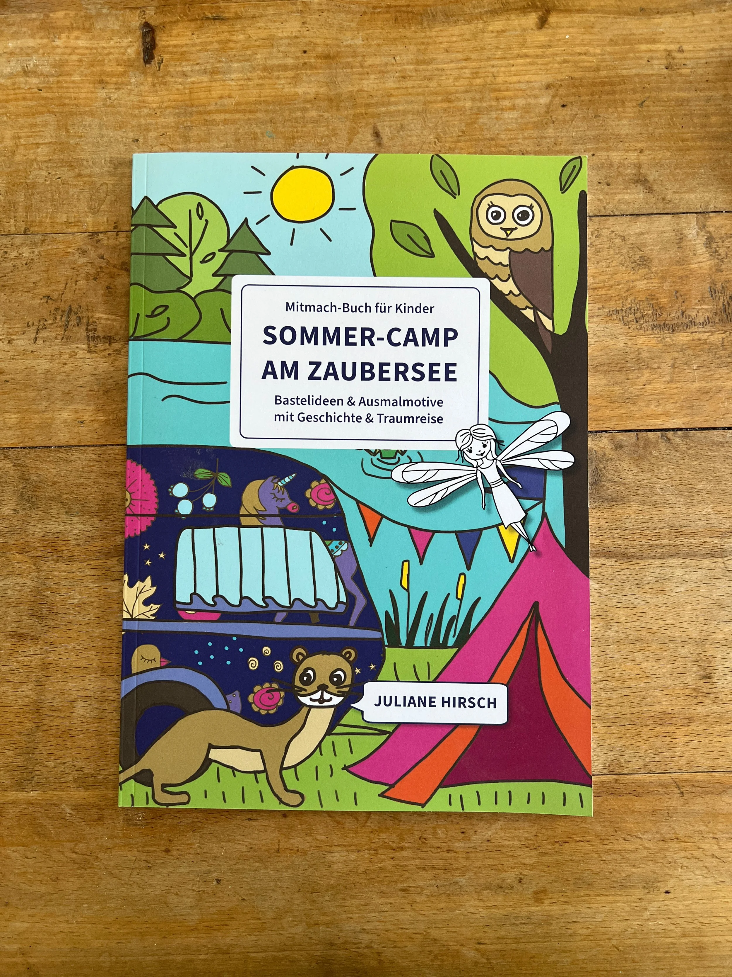 Bastelprojekt einer Puppenbühne aus einer Kartonbox mit bunten Blumenstoffen, einem Papiereinhorngriff und einer Miniaturfigur, umgeben von farbigem Papierdekor mit einem Baum und Blumen. Text auf einem Aufkleber in der Mitte: "Alles möglich Welt".