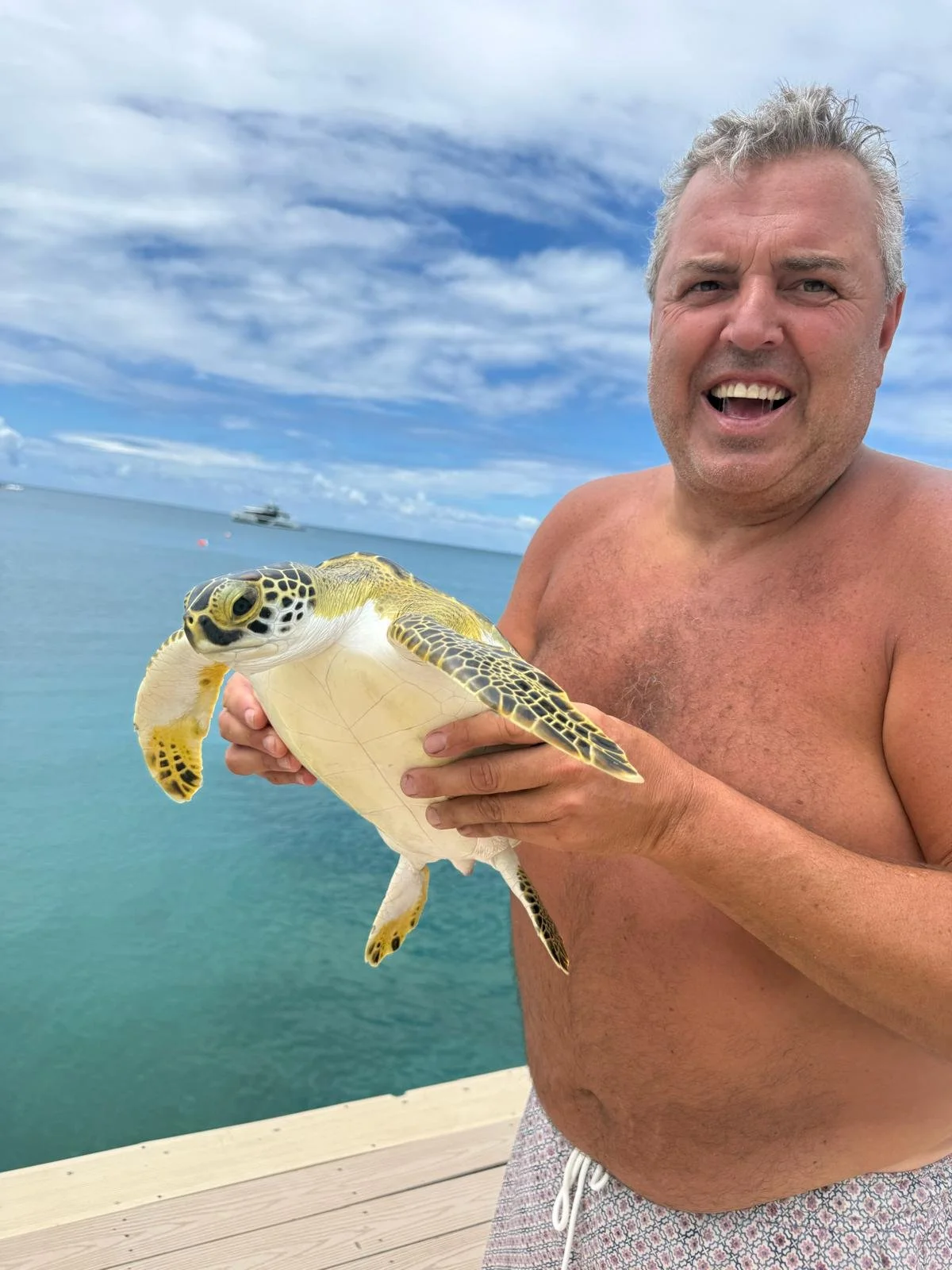 A man holding a sea turtle by the beach with ocean and sky in the background.