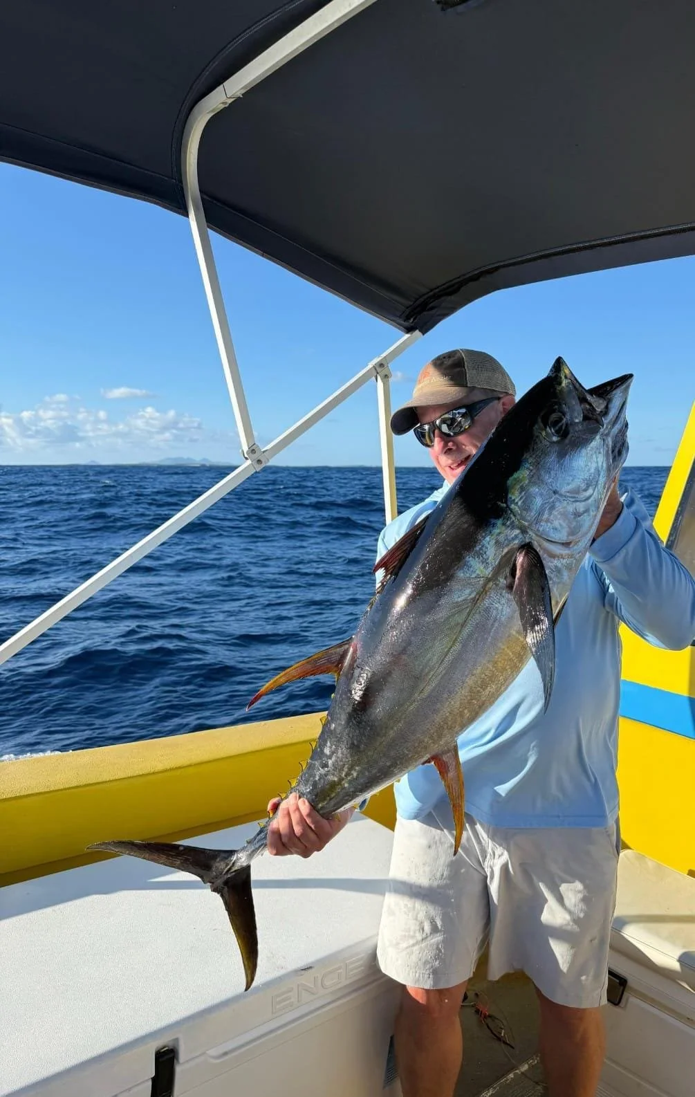 Man holding large fish on a boat in open water with blue sky and ocean in background.