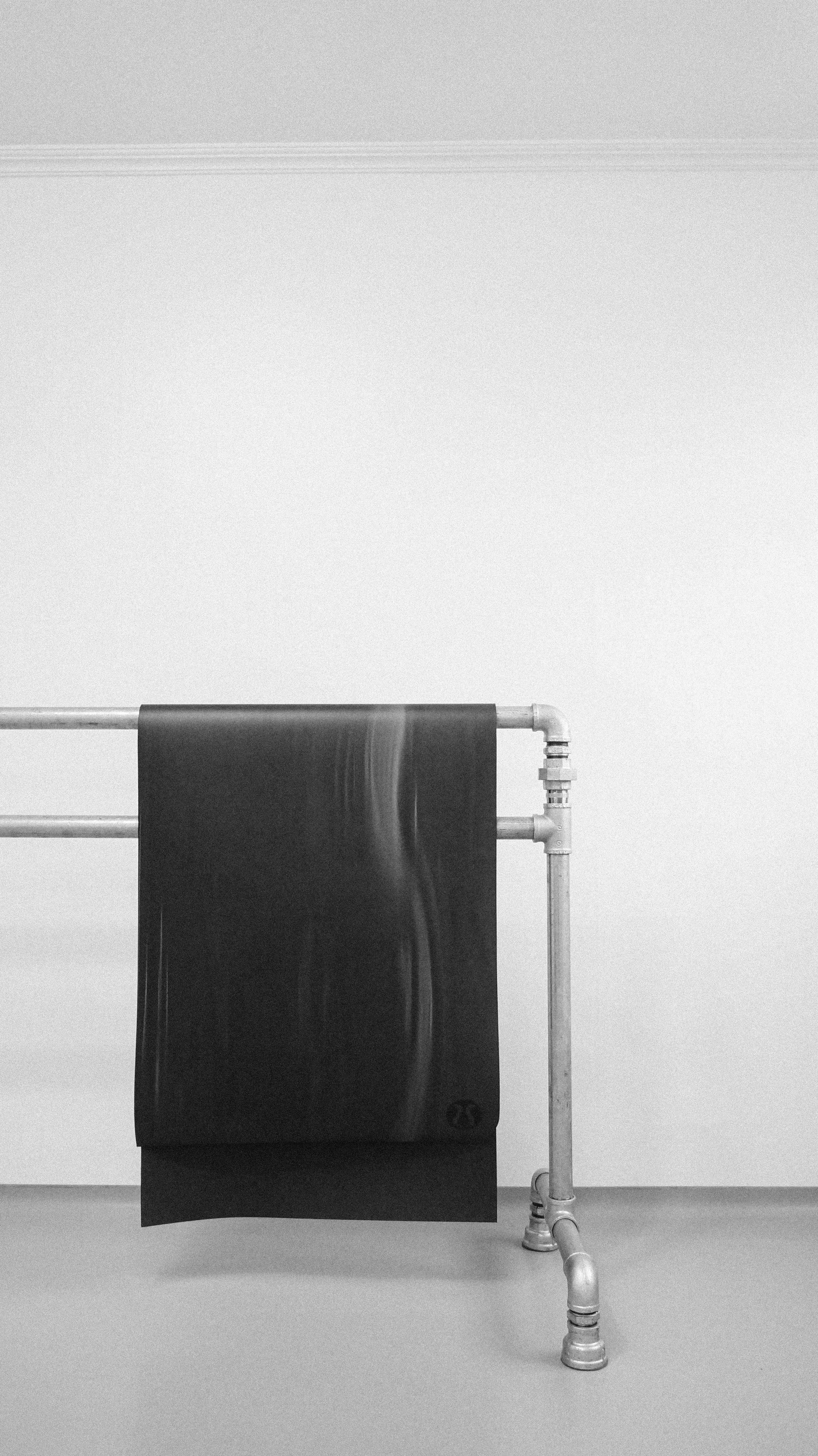 Black yoga mat hanging on a metal rail against a white wall