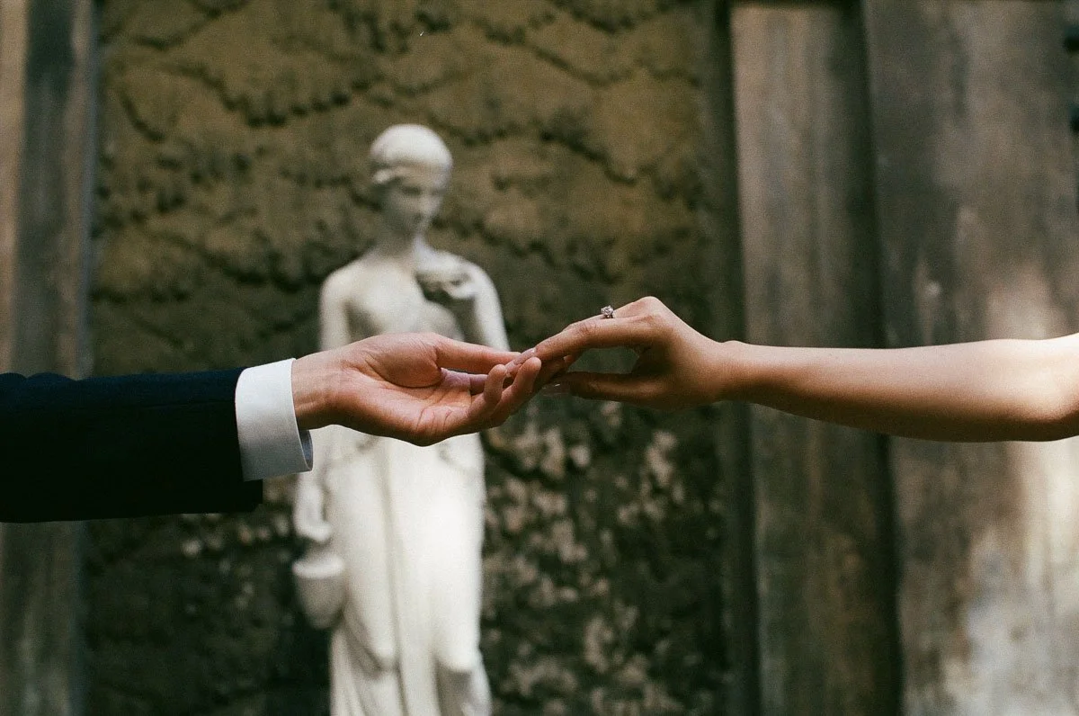 Copenhagen Wedding Photographer. A man in a suit holding hands with a woman with a ring on her finger in front of a classical statue of a woman.