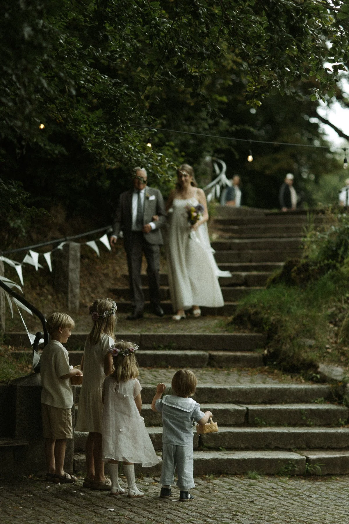 A wedding scene outdoors with children in the foreground watching the bride and groom descend steps.