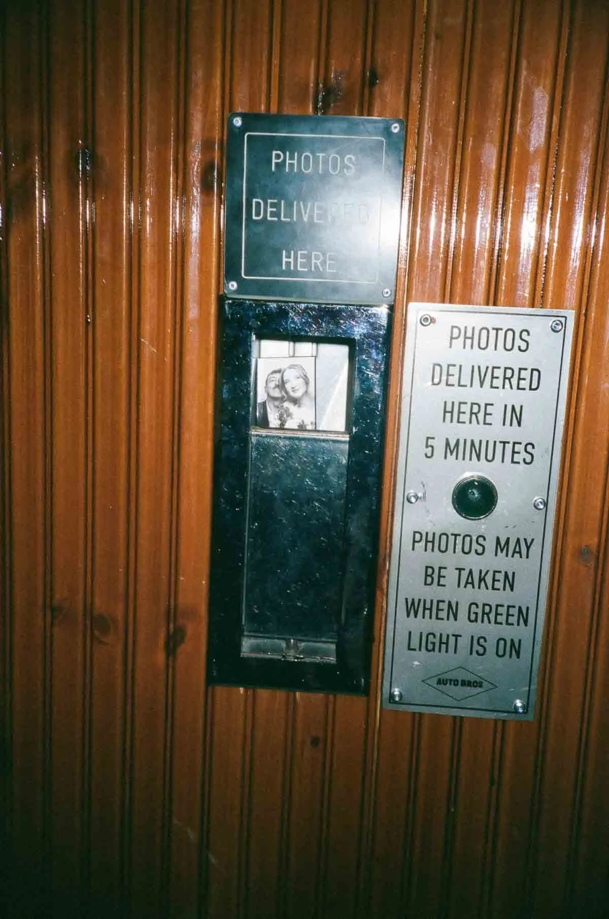 Photo booth with signs indicating photos are delivered here in 5 minutes and may be taken when green light is on.
