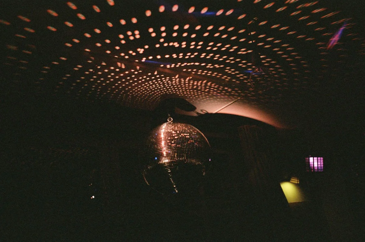 Disco ball hanging from the ceiling reflecting light, with a dotted light pattern on the ceiling and dark background.