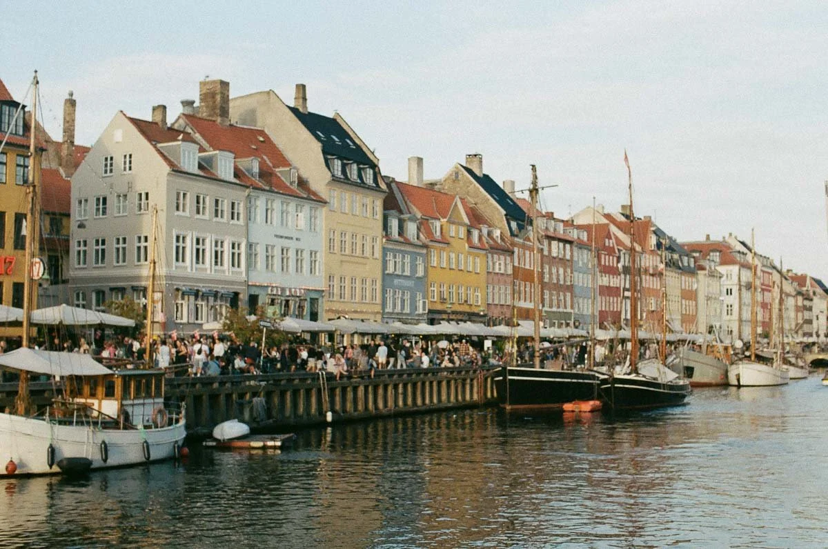 Copenhagen Wedding Photographer. Colorful buildings along a waterfront with boats docked, crowded with people