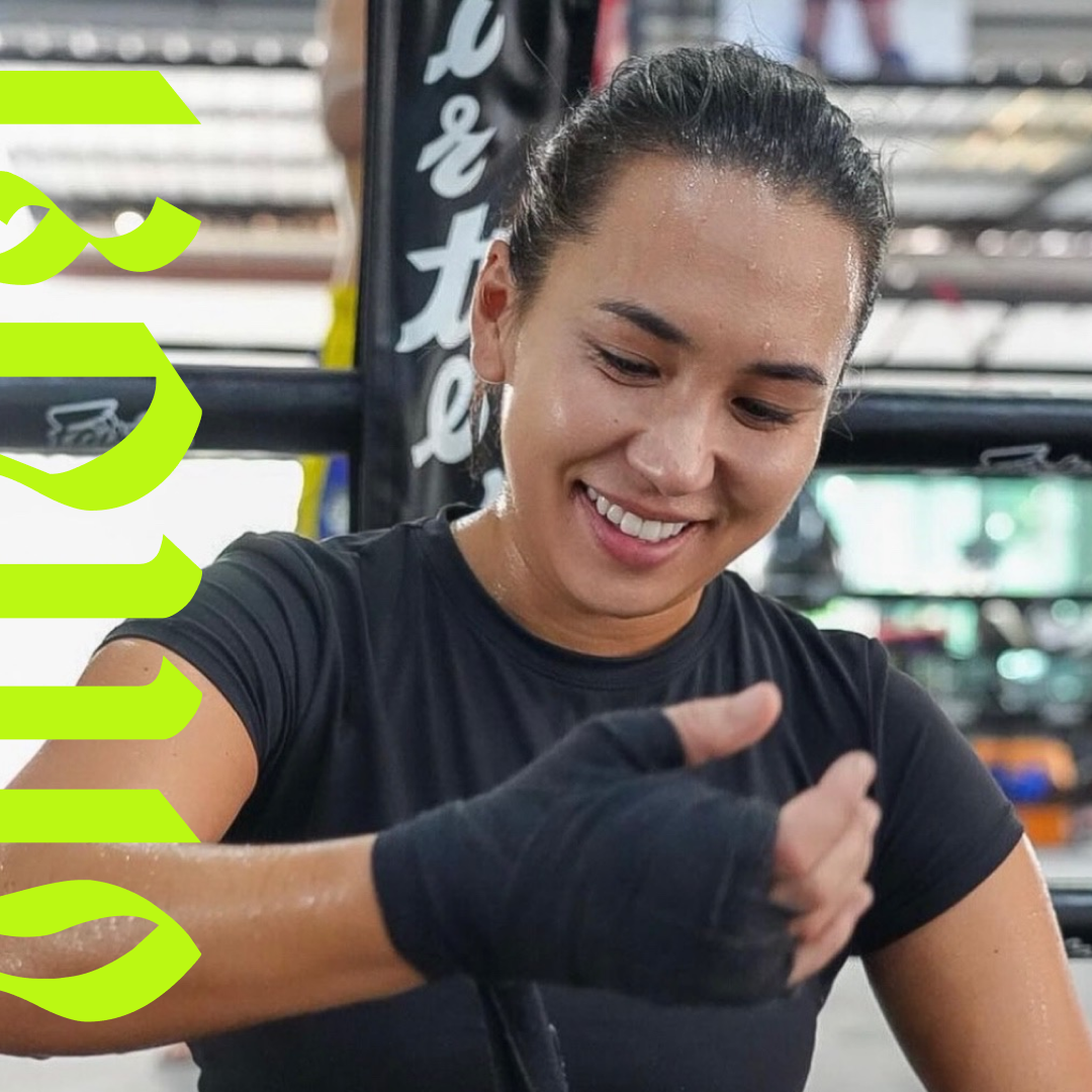 A young woman in workout attire smiling and wrapping her hands with boxing hand wraps in a gym.