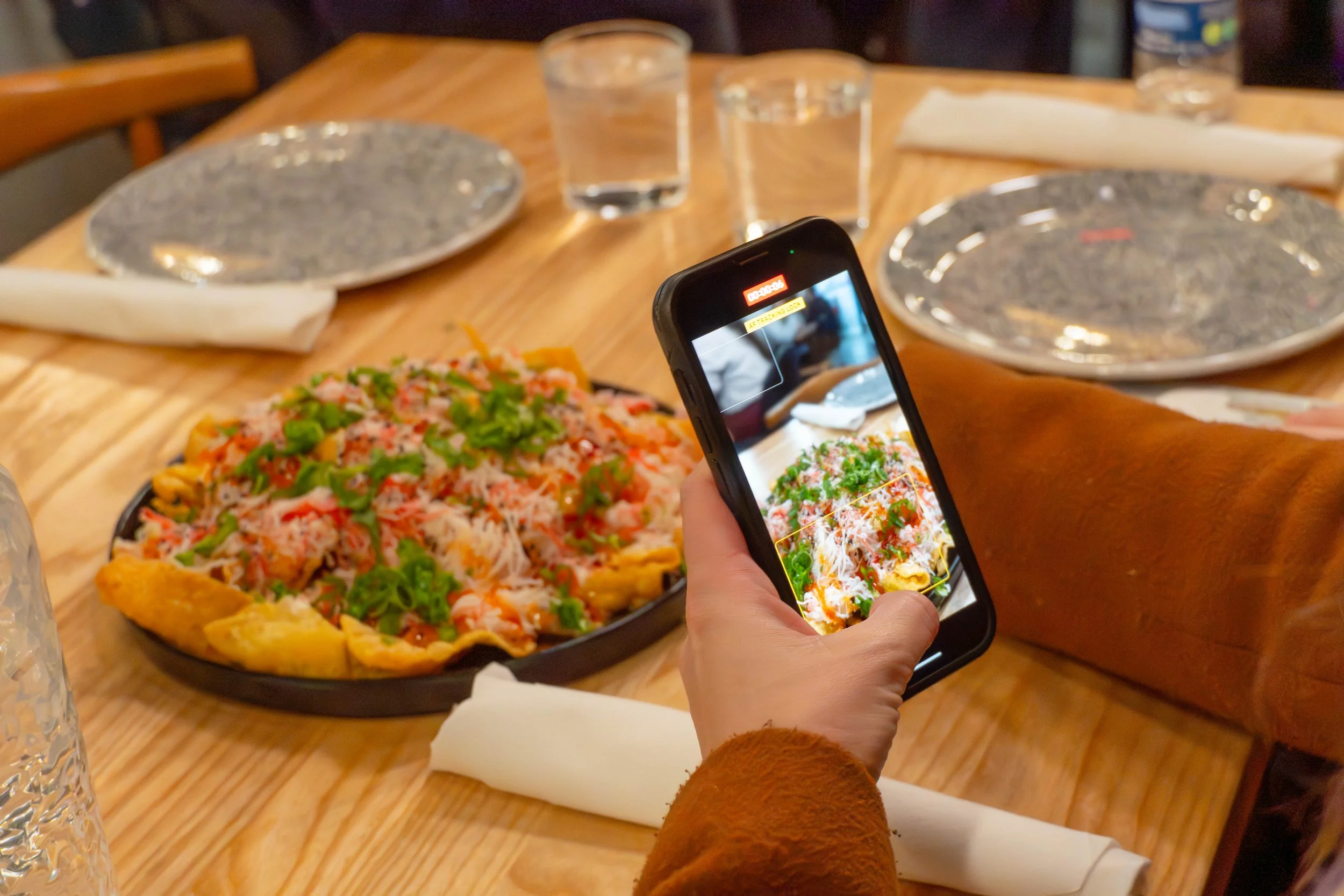 Person taking a photo of a seafood pizza at a restaurant table.