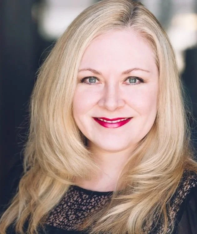 Portrait of a woman with long blonde hair, blue eyes, red lipstick, and wearing a black lace top.