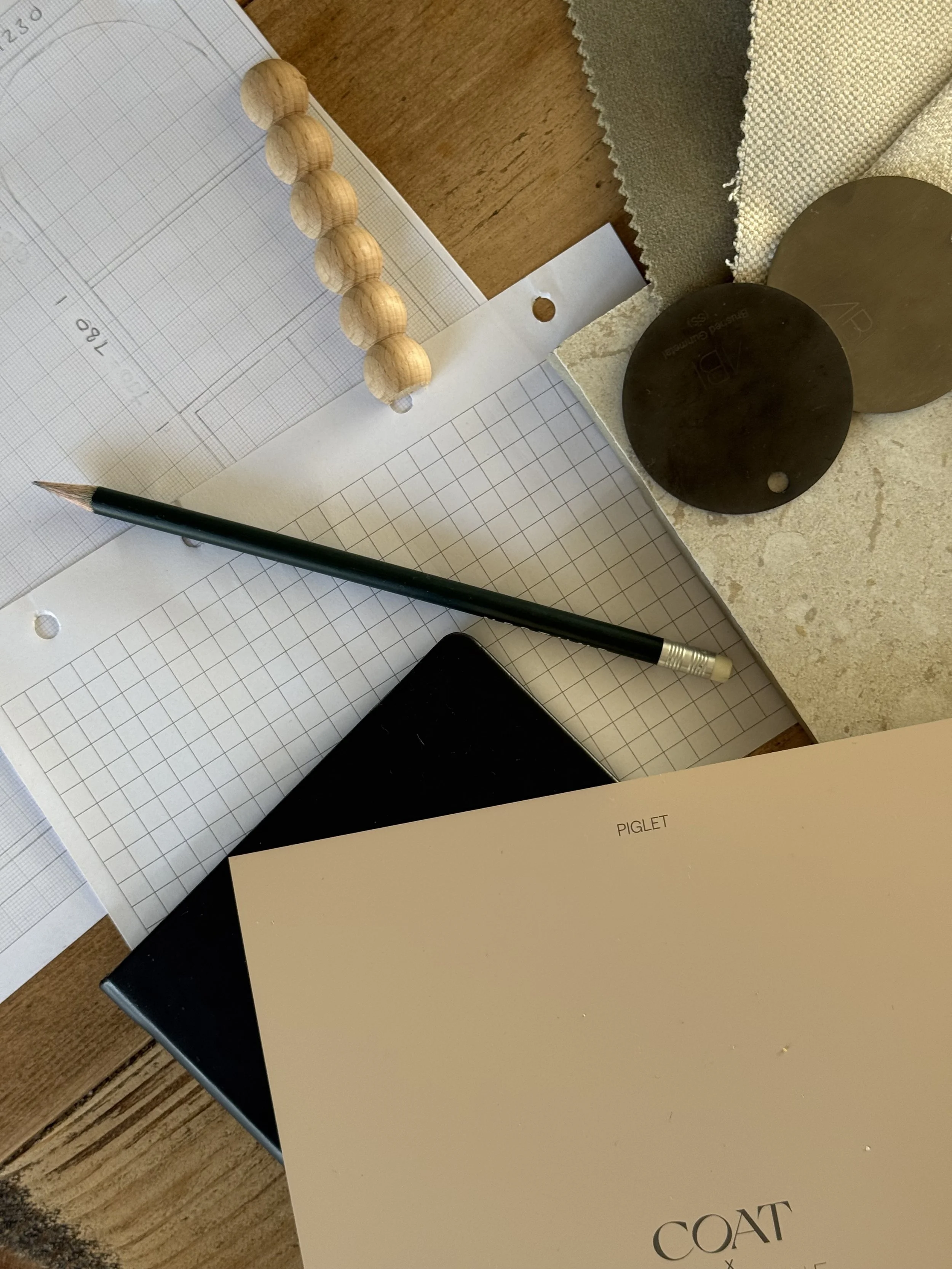 A selection of items used by an interior designer including graph paper, a pencil, a notebook, a paint sample, metal and tile samples