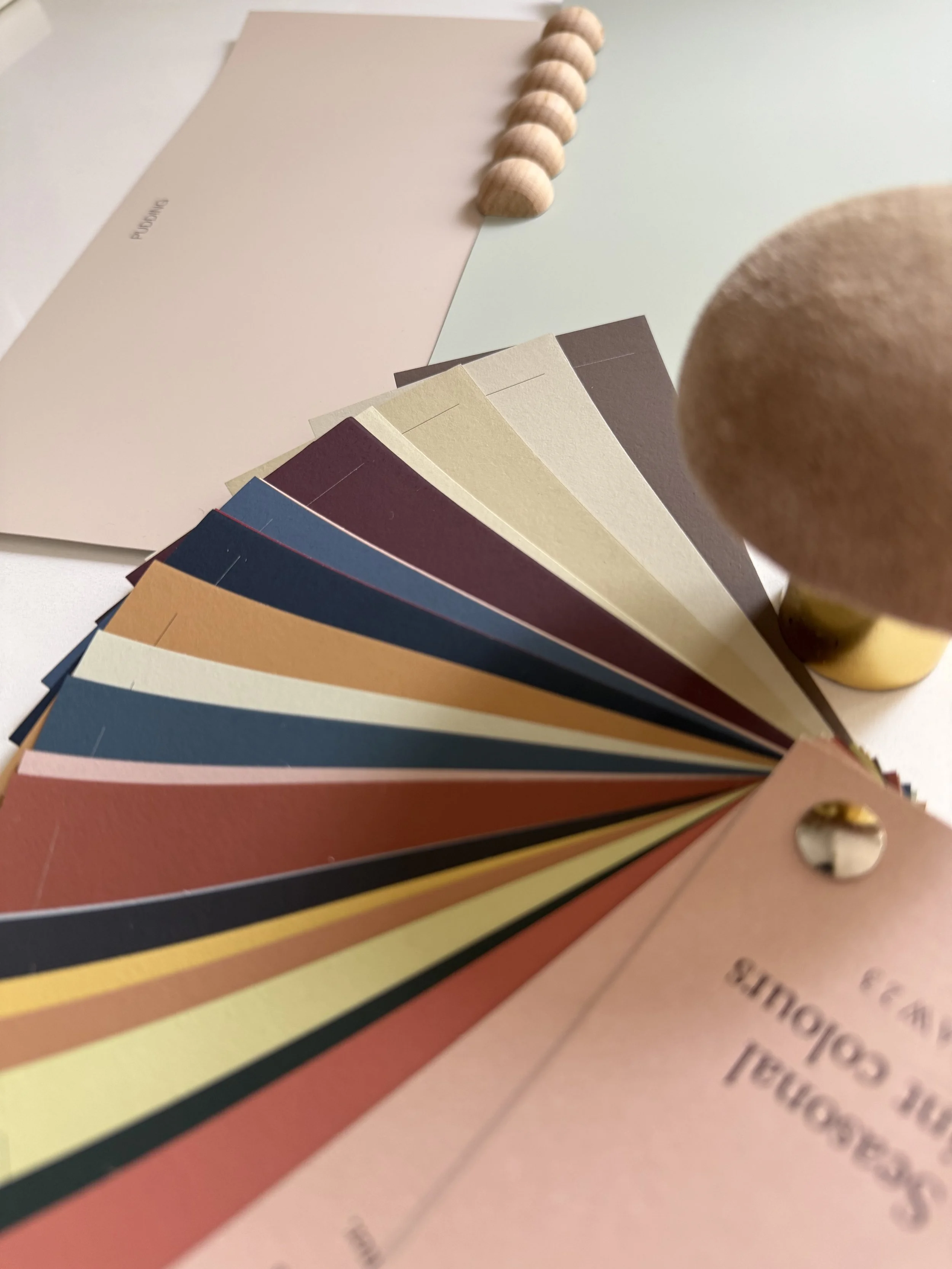 A paint fan deck of various colours alongside other interior design mood board accessories