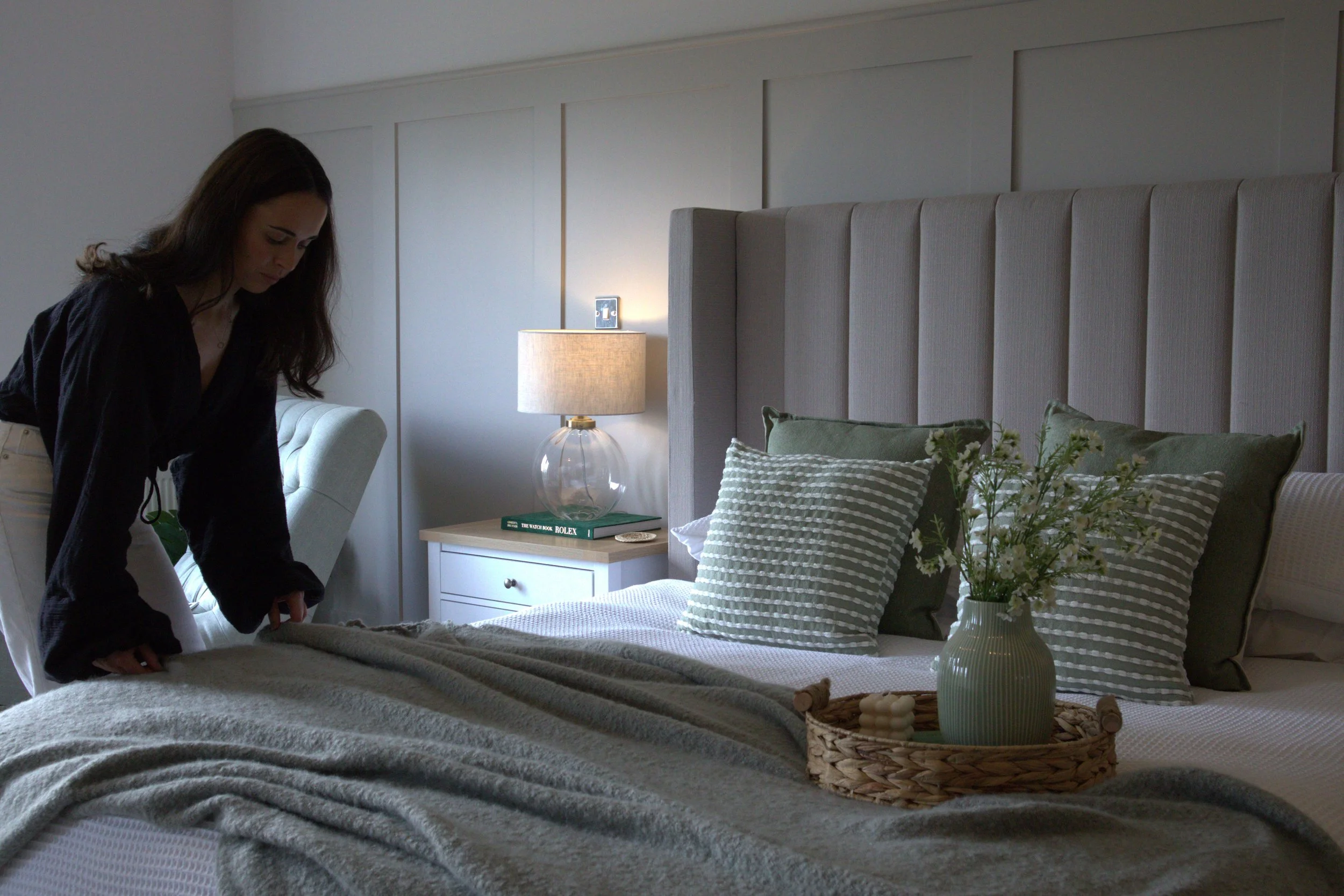 Interior designer in a neutral bedroom styling the bed with throws and cushions