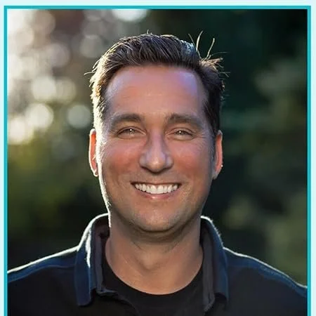 A smiling man outdoors with a blurred natural background and a teal border.