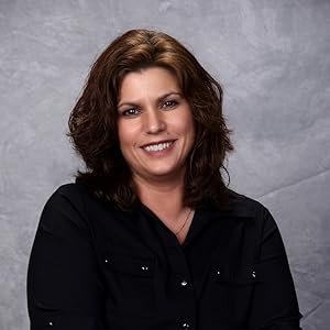 A woman with shoulder-length brown hair, wearing a black shirt, smiling at the camera against a gray background.