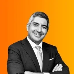 A man in a suit smiling with his arms crossed against an orange background.