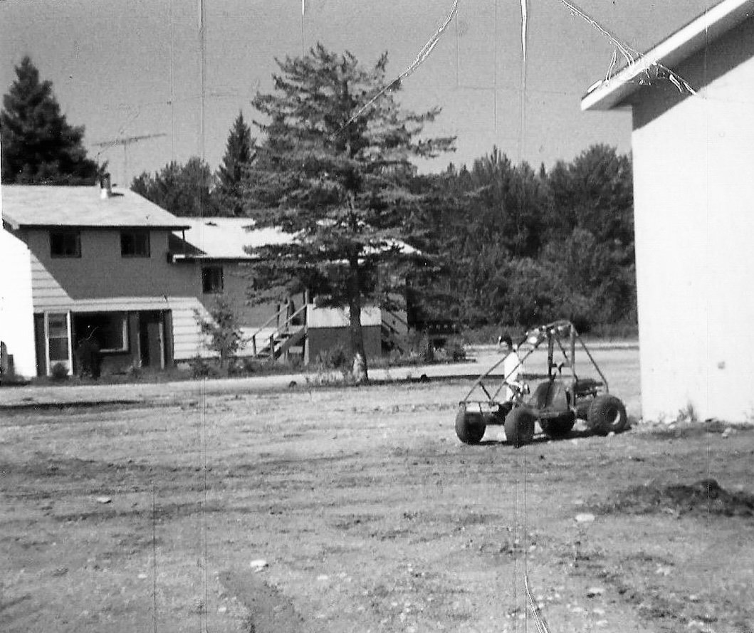 Black and white photo of a young Vinessa Redford standing next to an off-road vehicle on a dirt lot with a house in the background in rural northern Alberta.