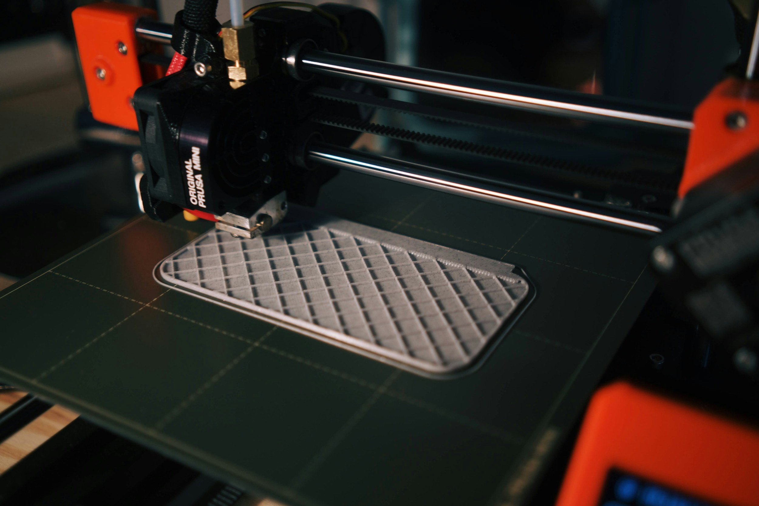 A 3D printer printing a gray object with a lattice pattern on a black build plate.