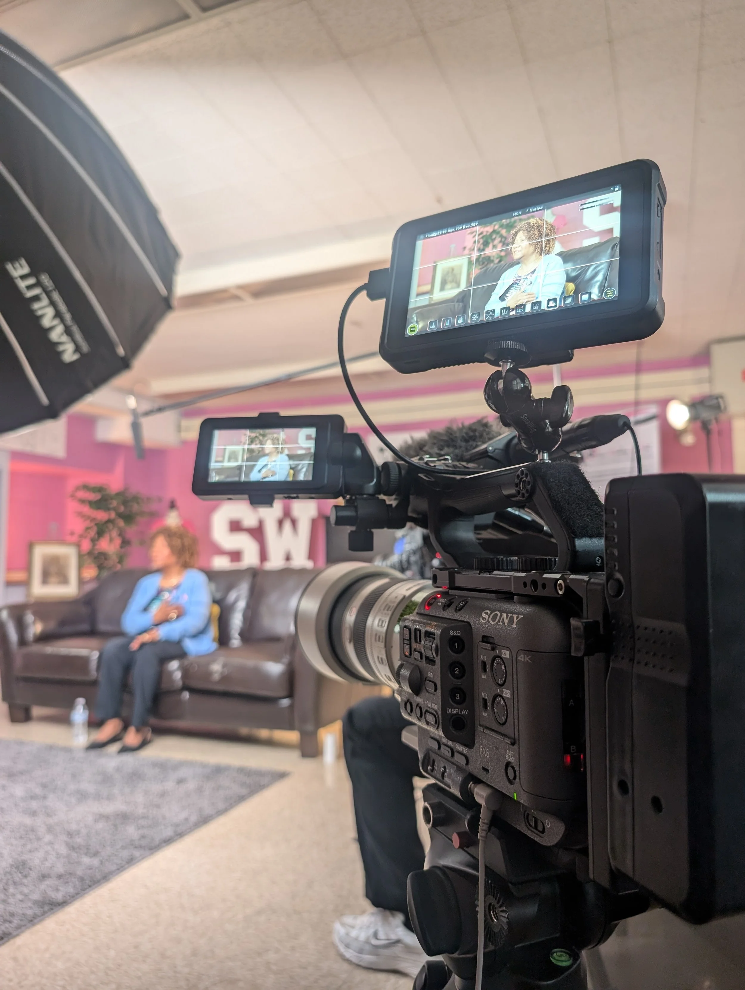 A professional video camera capturing a woman sitting on a sofa during an interview or talk show.