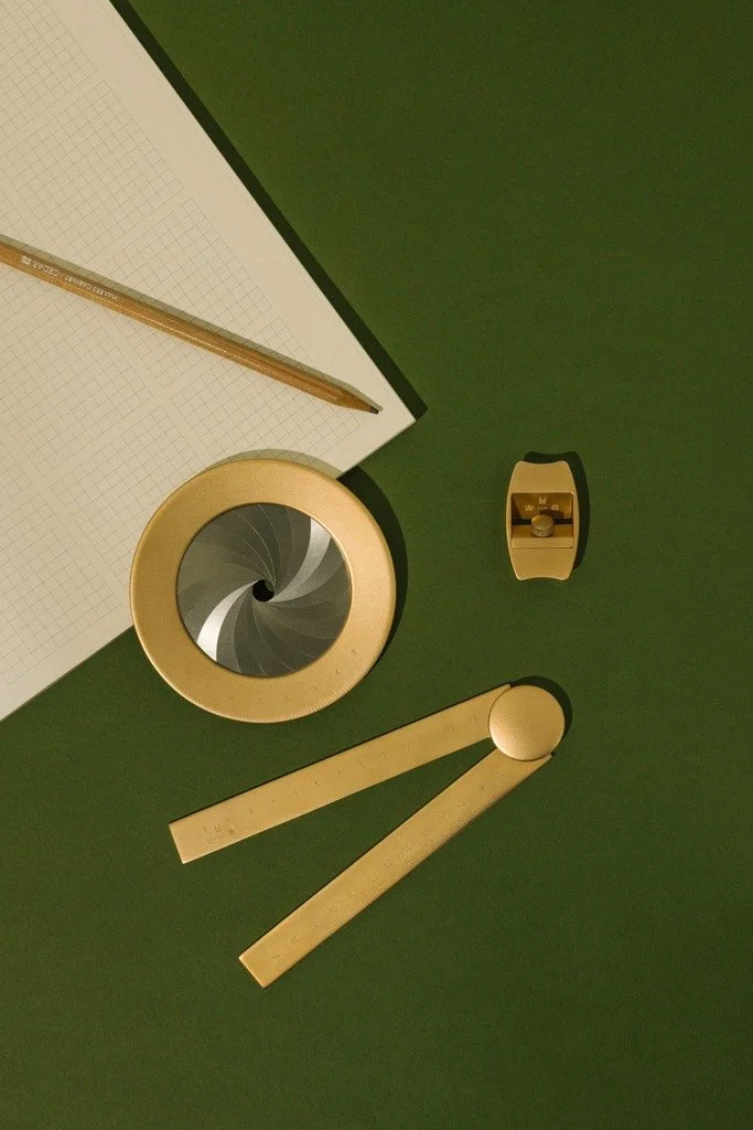 Flat lay of stationery items on green surface, including a pencil, grid paper, sharpener, and drawing tools