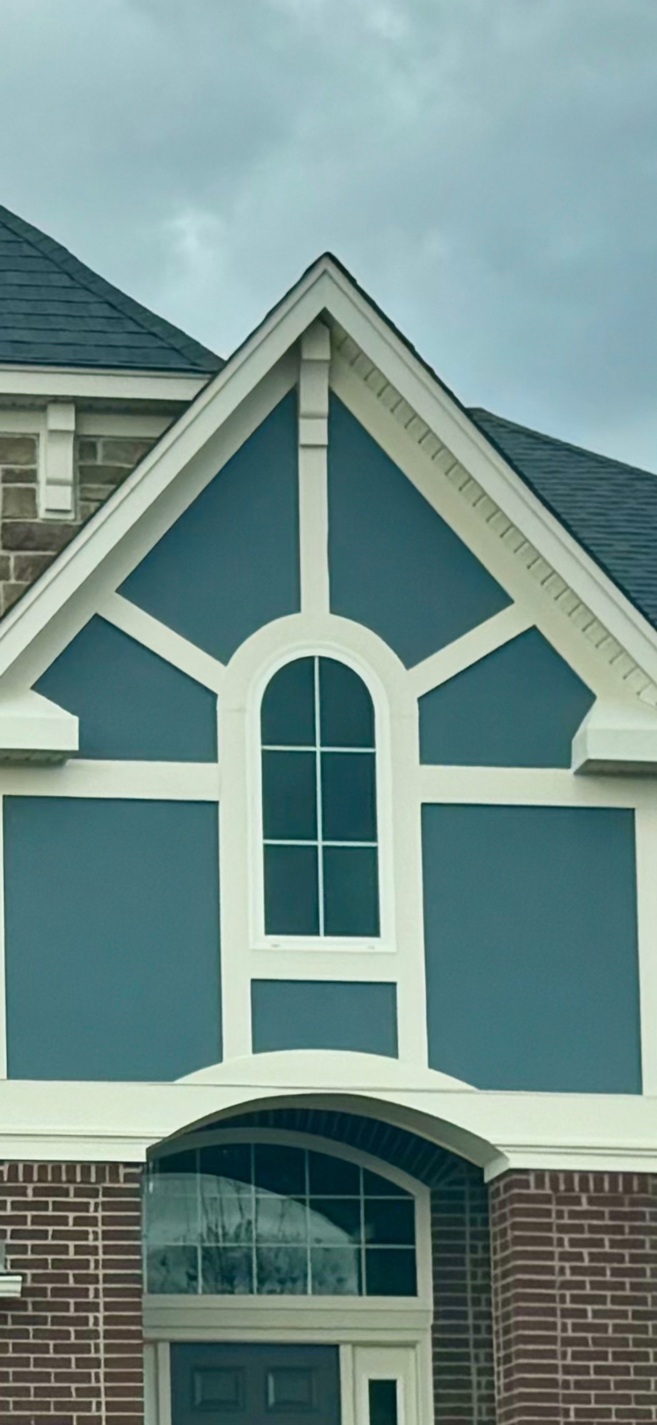 Front exterior of a house with a brick lower section, a sail-blue upper section, and a large arched window with smaller window panes in a cross pattern.