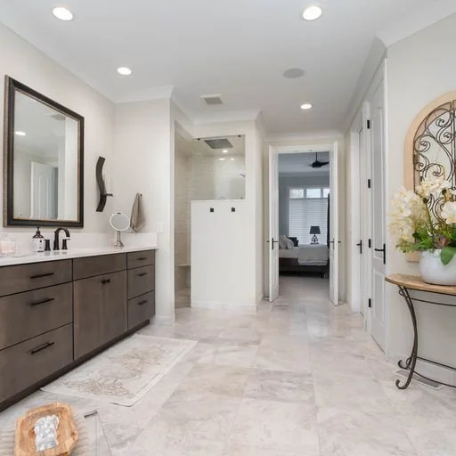 Modern bathroom with double vanity, large mirror, and neutral color palette, leading to a bedroom with a ceiling fan.