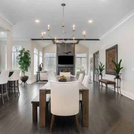 Modern dining and living room with white walls, dark hardwood floors, a chandelier, a wall-mounted TV, and large windows.