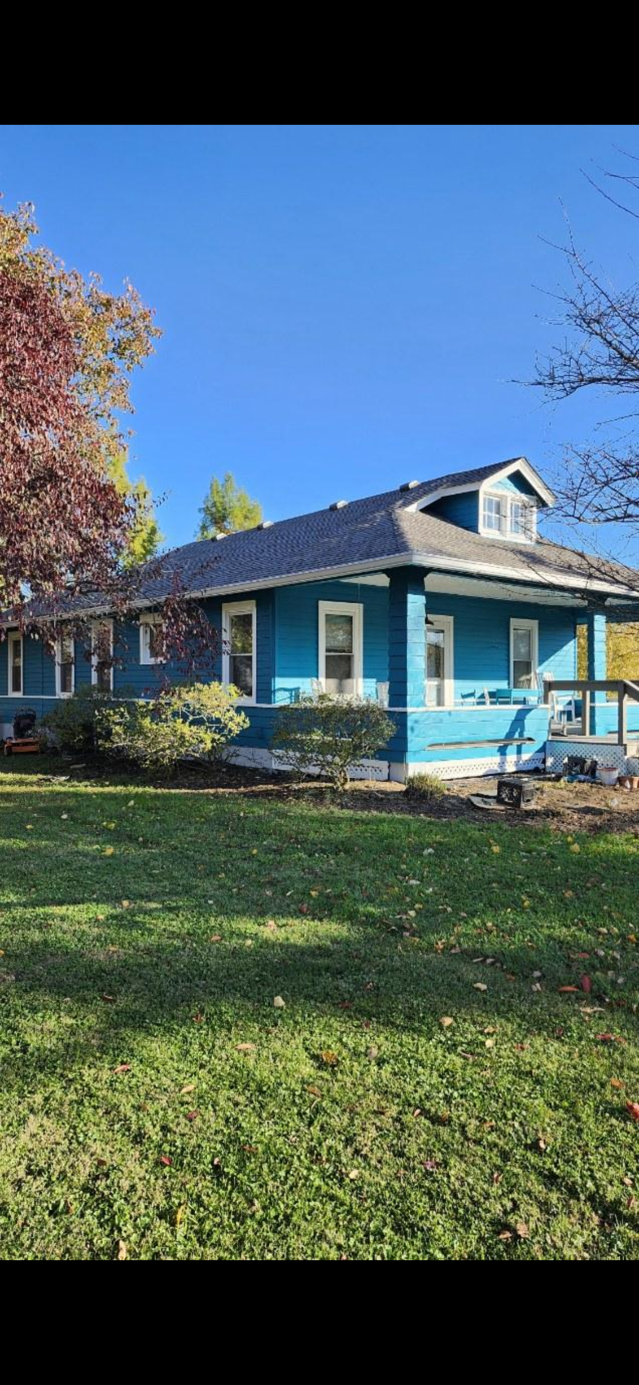 A blue house with white trim, a small porch, and a gable window, surrounded by green grass and trees with colorful autumn leaves.