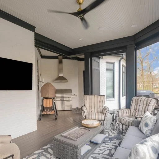 Living room with striped armchairs, a gray sofa, a coffee table, a grill, and large windows with a view of trees outside.