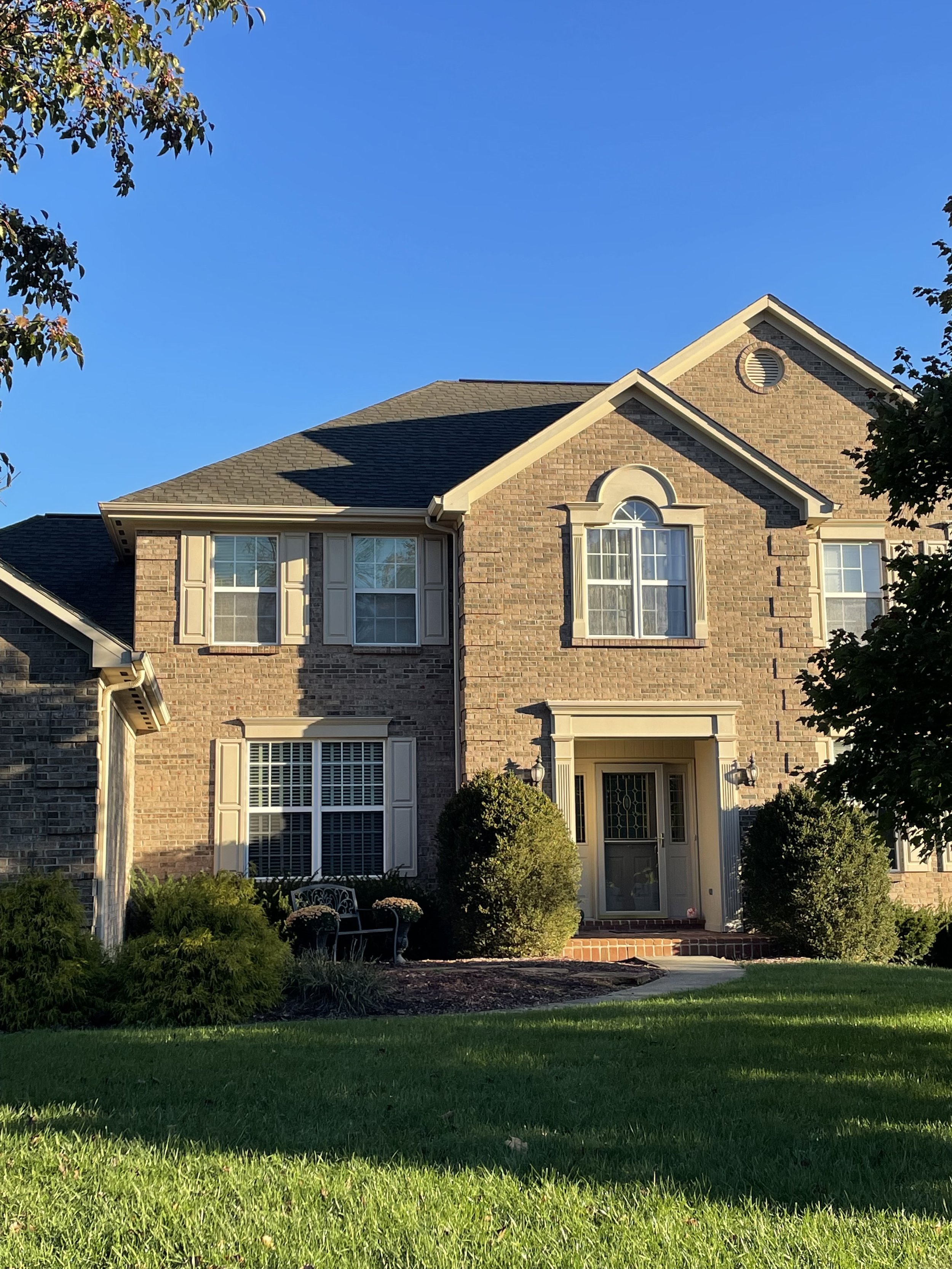 Front view of a two-story brick house with white trim, a door with a decorative glass panel, multiple windows, and a well-maintained lawn with bushes and a walkway.