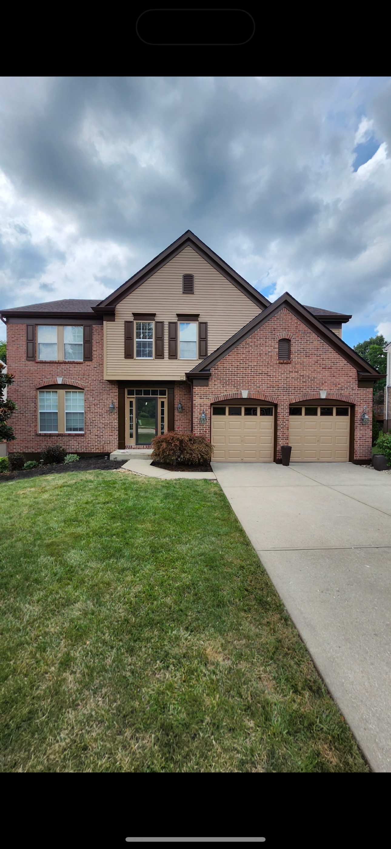 Two-story house with a brick and beige vinyl siding exterior, two attached garage doors, front porch, windows with shutters, and a well-maintained lawn with a curved walkway.