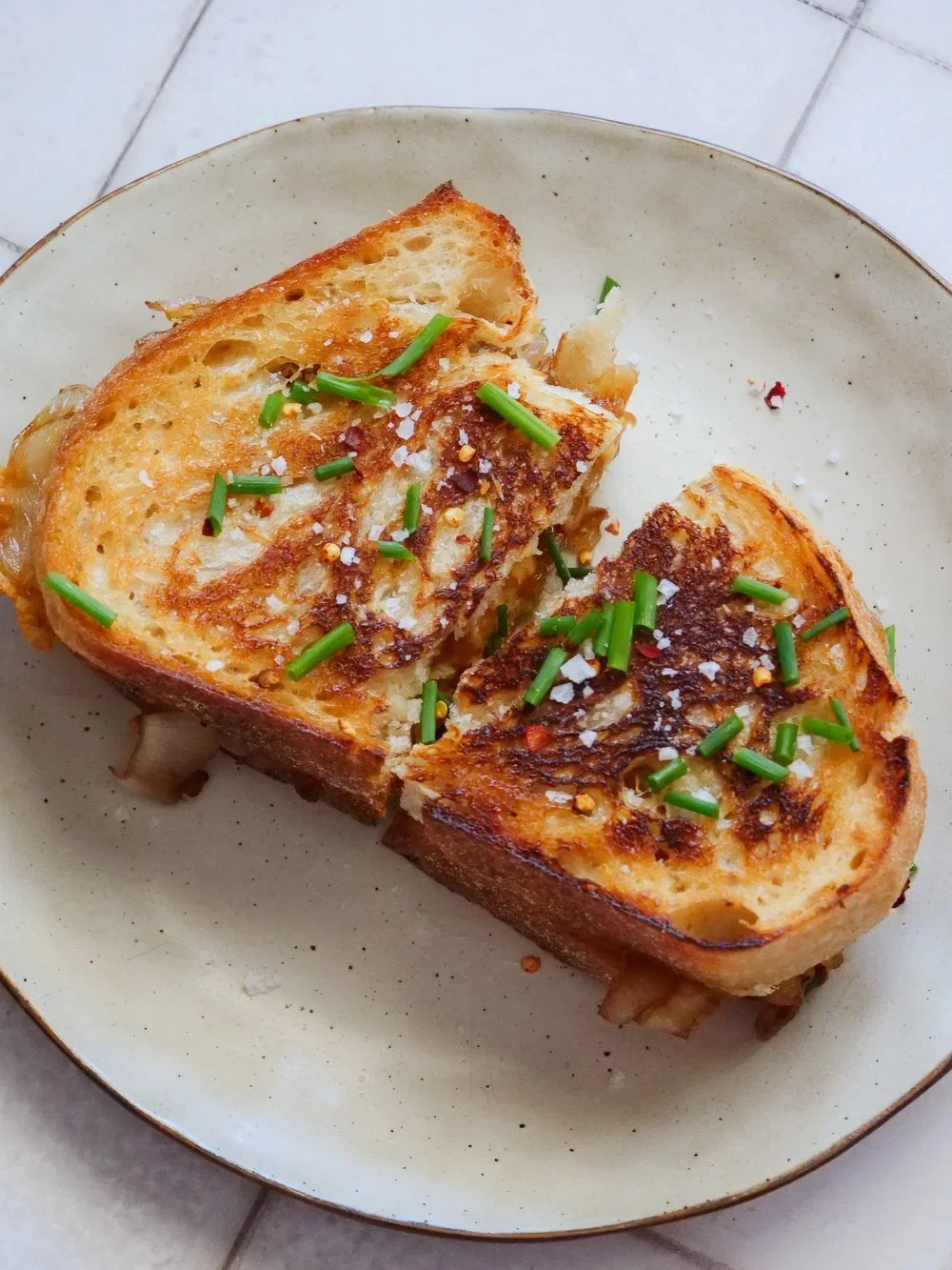 Two slices of French toast garnished with chopped green onions and salt on a white plate.