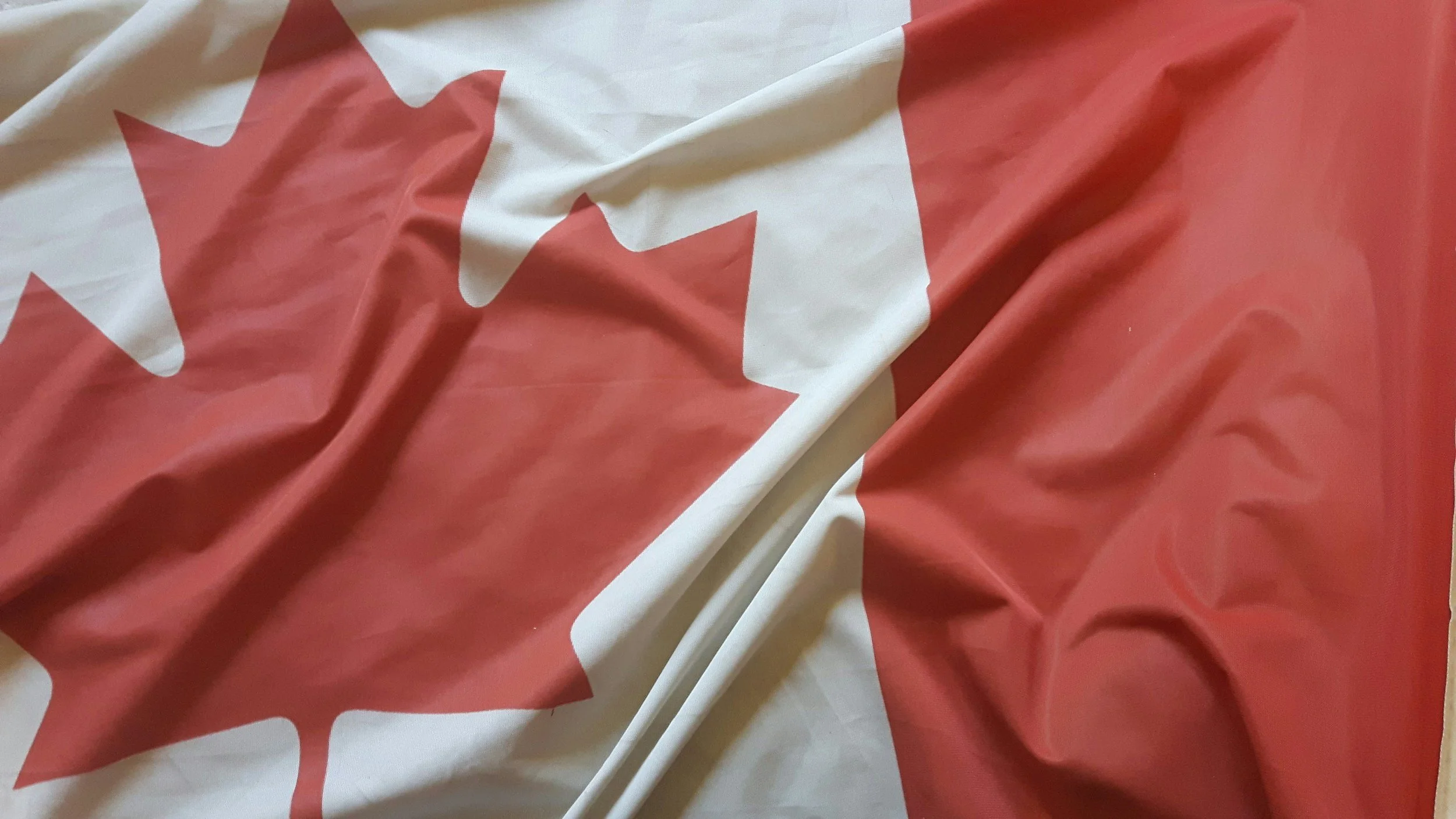 A close-up of a Canadian flag with a red maple leaf on a white background, slightly wrinkled.