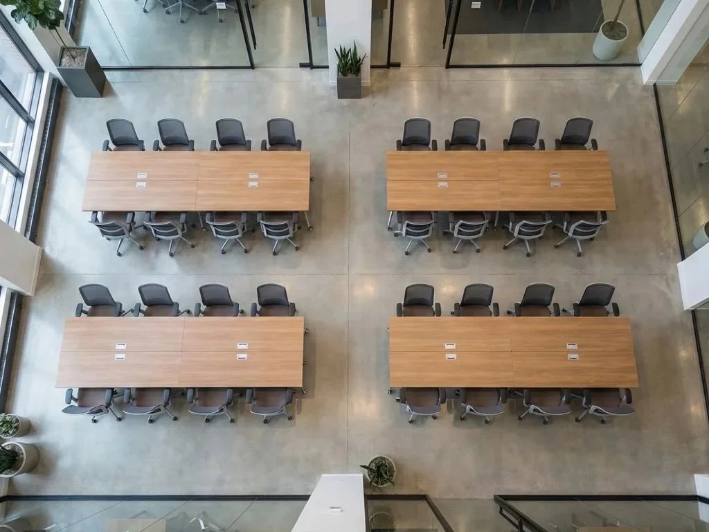 Four rectangular wooden conference tables with black chairs arranged around them in a modern office space.