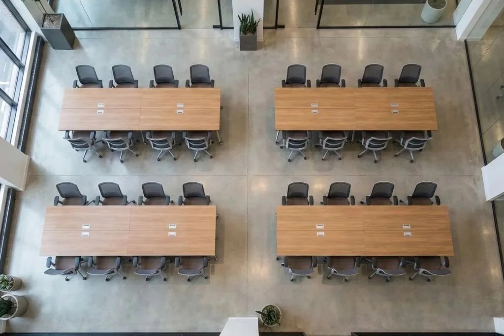 Overhead view of four large conference tables with black chairs in a modern office space.