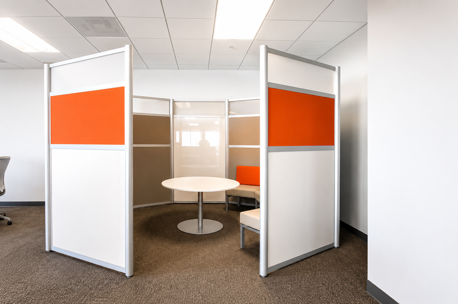 Empty office cubicles with orange, beige, and brown panels, a round white table, and a partial office chair, in a modern office space.