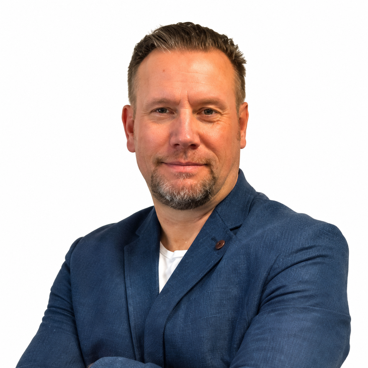 Professional man with short hair, beard, wearing a blue blazer, smiling with arms crossed, white background.