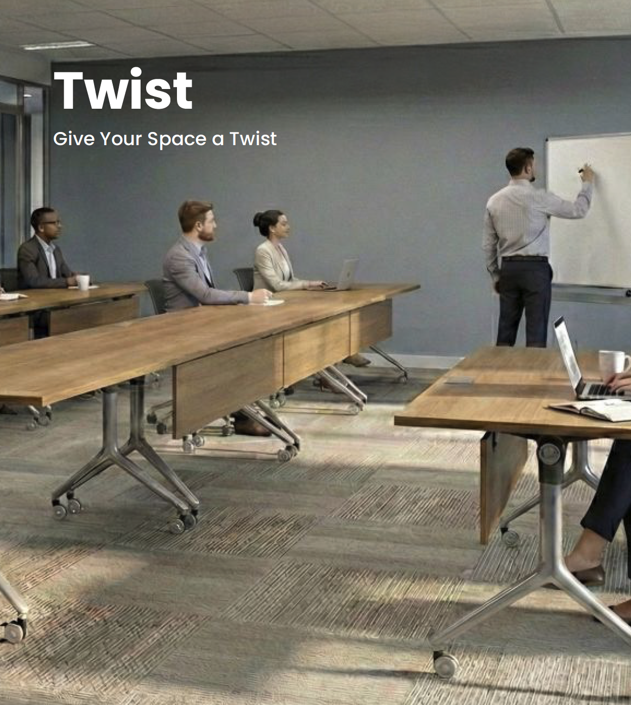A business meeting or classroom setting with four people sitting at wooden tables, one person standing and writing on a whiteboard. The tables are on caster wheels, and some people have laptops and notebooks.