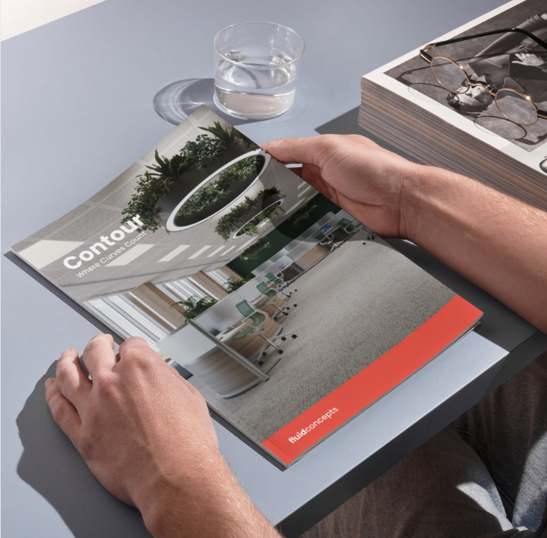 Person flipping through a magazine about architectural design, with a glass of water and a stack of magazines on the light blue table.