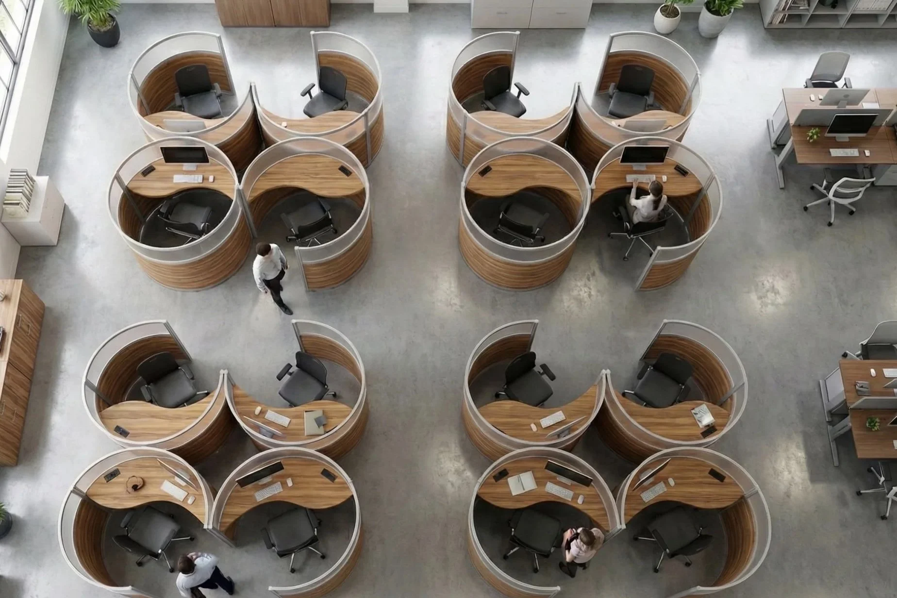An aerial view of a modern office space with multiple semi-circular private work pods arranged in a grid pattern. Each pod has a wooden desk, a black office chair, and some have computers and other office supplies. There are four people walking or working in the pods, and a few potted plants are visible around the space.