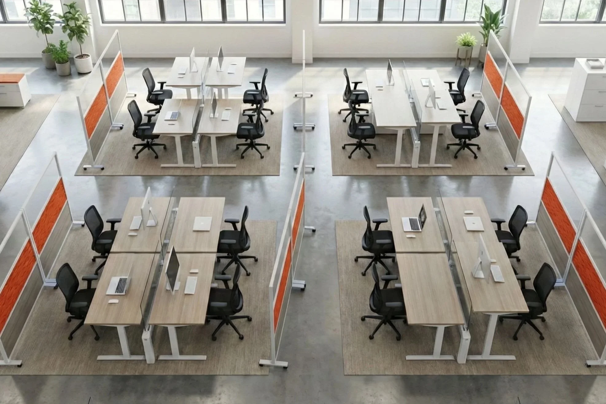 An open-plan office with multiple work desks arranged in a grid pattern. Each desk has a computer and a black office chair. There are glass dividers between desks and potted plants along the large windows in the background. The room has a concrete floor and a modern, minimalistic design.