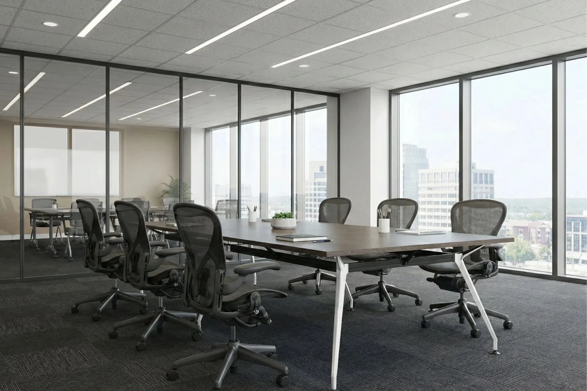 Modern conference room with a large table, black ergonomic chairs, and floor-to-ceiling windows showing city buildings.