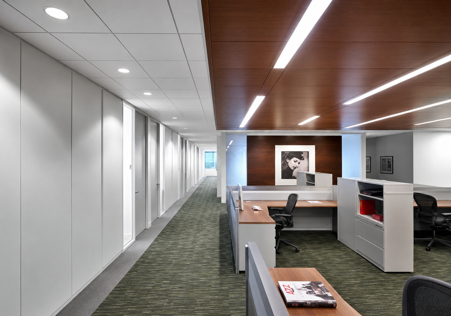 Empty modern office space with desks, chairs, and a hallway leading to a window.