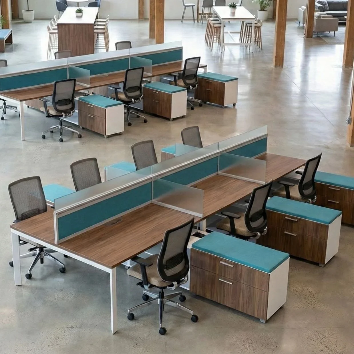 Open-plan office space with multiple desks separated by teal and glass dividers, ergonomic chairs, and wooden storage cabinets, with additional tables and sitting areas in the background.