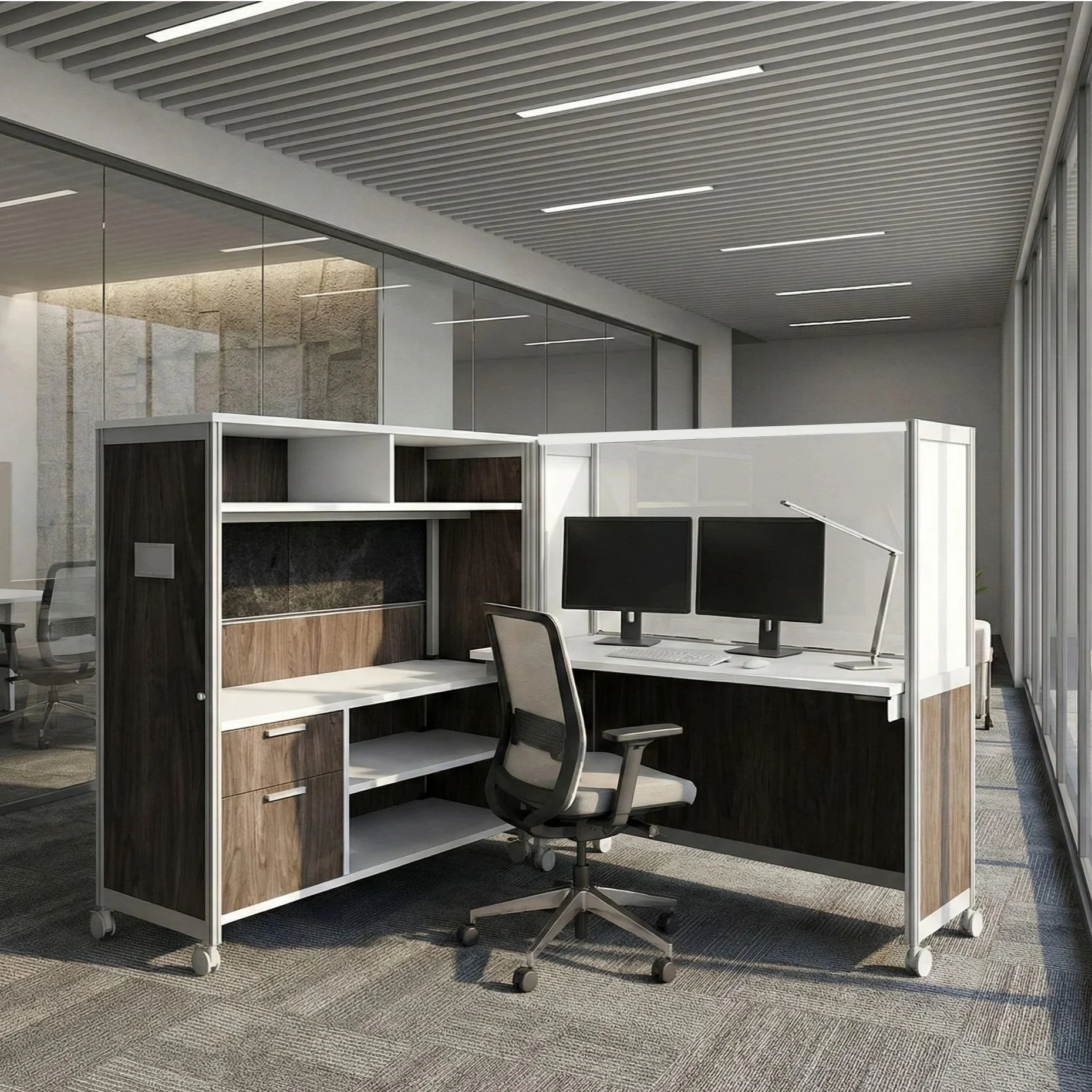 Office cubicle with a black swivel chair, dual computer monitors, and wooden cabinetry, separated by glass walls, in a modern and brightly lit workspace.