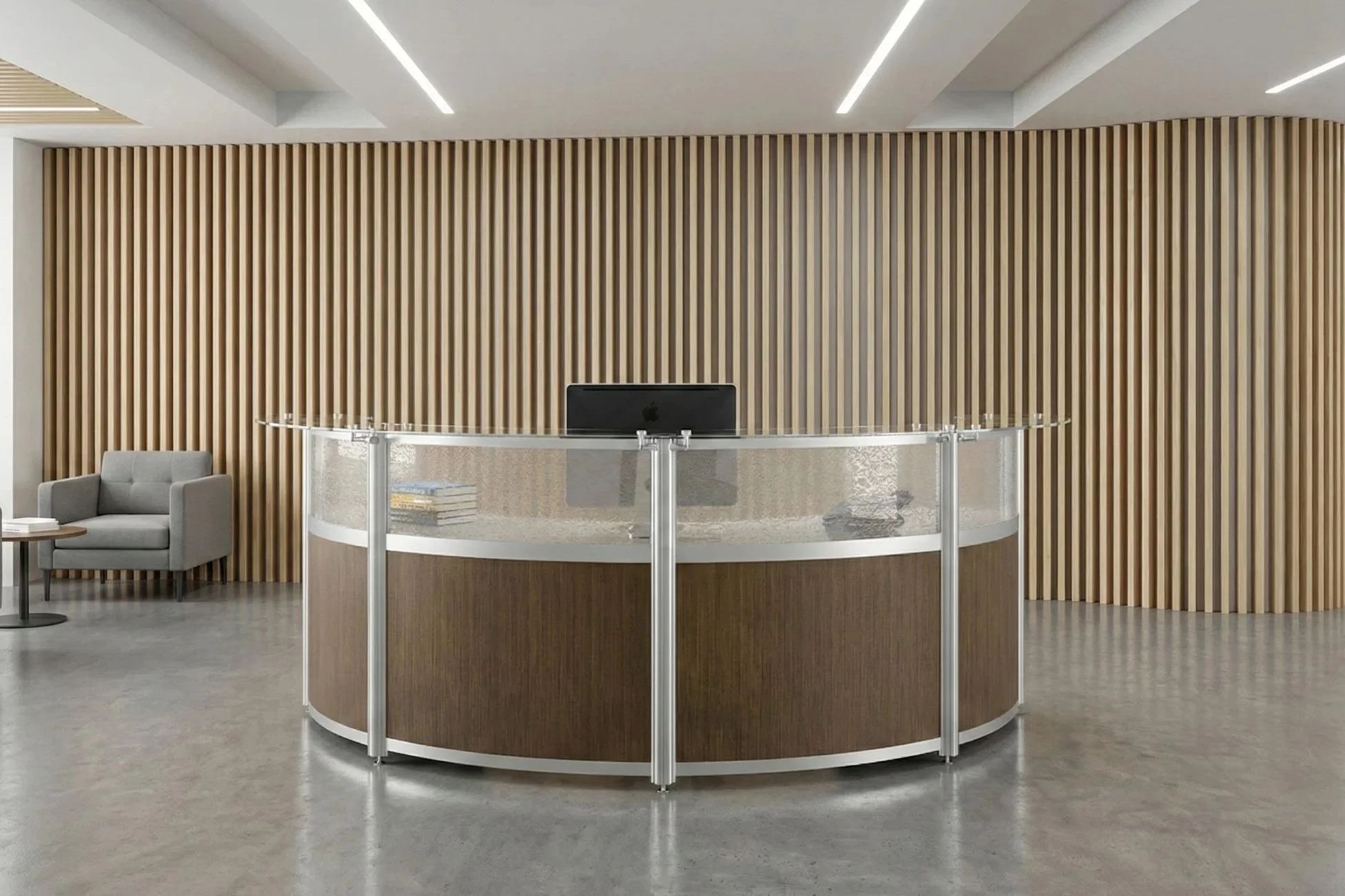 Modern reception area with a curved desk, a computer, books, a gray armchair, and a wooden slat wall background.