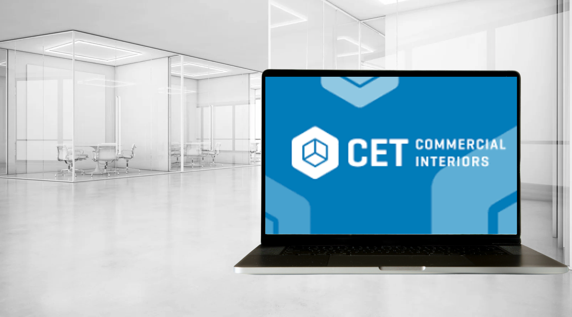 Modern empty office space with glass conference rooms and a laptop displaying the CET Commercial Interiors logo on its screen.