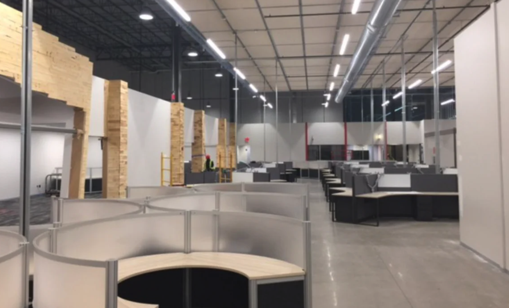 Empty office space with cubicles, modern design, and construction workers adding materials to the wall.