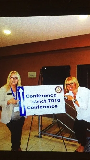 Joanna Cox and LIz Spooner posing with a Rotary District Conference sign